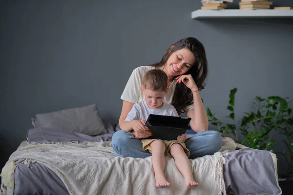 Anya és fia tablettel otthon. Anya mutatja média tartalom on-line a fiának egy tabletta a nappaliban egy ház belsejében — Stock Fotó