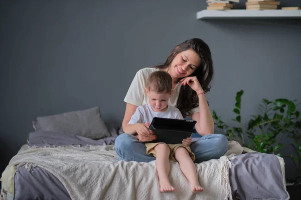 mother and son with tablet at home. Mother showing media content on line to her son in a tablet in the living room in a house interior