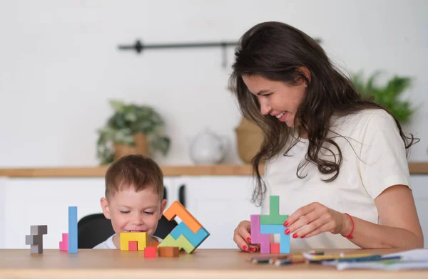 子供の男の子と母親が家のテーブルでおもちゃを遊んでいます。テーブルの上でカラフルな木製のレンガで遊ぶ子供たちは. — ストック写真