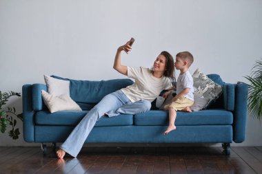 Anne oğluyla selfie çekiyor evdeki oturma odasında bir kanepede oturuyor.