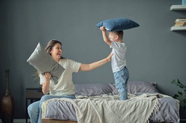 Anne, küçük oğluyla birlikte yatakta oynuyordu. Aile anları, çocukların bakımı. Annelik, çocuk saldırganlığı kavramı