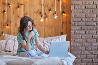 Güzel bir kadın yatakta oturuyor ve bir dizüstü bilgisayar üzerinde çalışıyor..