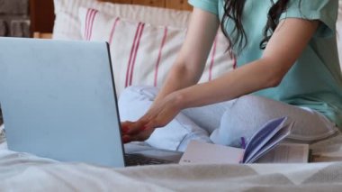 Kadın yatakta oturur ve dizüstü bilgisayarda çalışır.