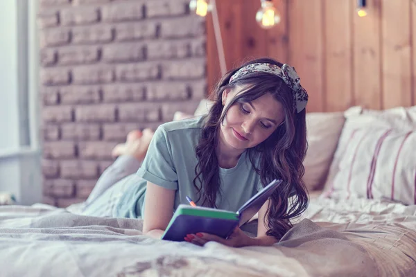 Estilo de vida imagem suave de uma jovem bonita sentada em sua cama acolhedora e fazendo anotações em seu diário. Temporada de outono humor. — Fotografia de Stock