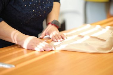 Elbise dikmek için tekstil işinde çalışan yetenekli bir kadın terzi. Dikiş işleminin görüntüsünü kapat. Işık bulanık arkaplan