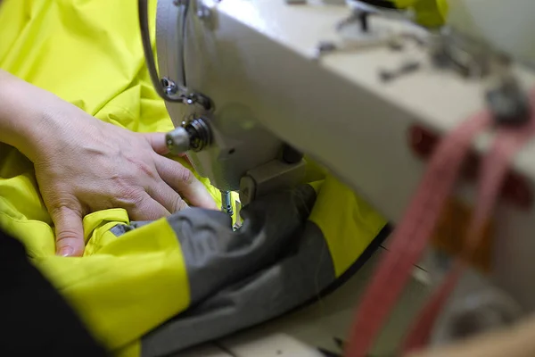 Female hands stitching white fabric on professional manufacturing machine at workplace. Close up view of sewing process. Light blurred background