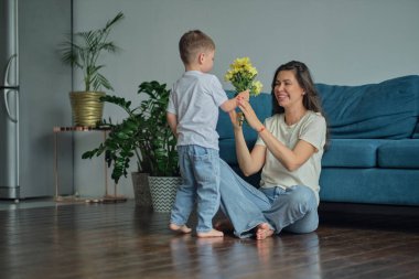 Anneler Günün kutlu olsun. Çocuk evlat tatilde annesini tebrik eder ve çiçek verir. Evde bayram kutlamaları sırasında anneler günü için onu tebrik etmek.