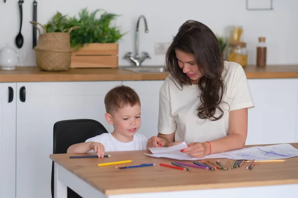 O rapazinho aprende a desenhar. Mãe e filho se divertem desenhando com lápis. Criatividade infantil. — Fotografia de Stock