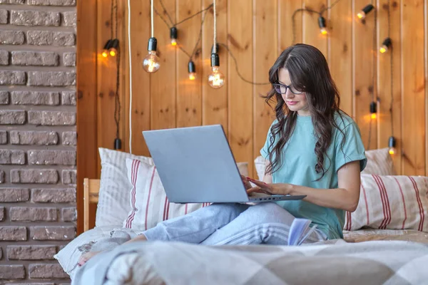 Bela mulher de meia idade está sentado na cama e trabalhando em um laptop. conceito de reciclagem de adultos, uma nova profissão após 30 anos — Fotografia de Stock