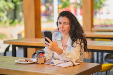 Gülümseyen neşeli, zarif, yaşlı kadın. Kafadan yakın plan, mutlu, orta yaşlı bir kadın kafede oturuyor ve bir arkadaşını bekliyor.