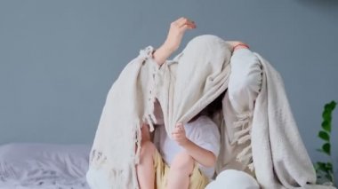 Anne ve çocuk yatak odasında, yatakta, battaniyenin altında eğleniyorlar. Küçük oğluyla birlikte hafta sonu yatakta oynayan genç bir anne. Tembel bir sabah, sıcak ve rahat bir ortam..