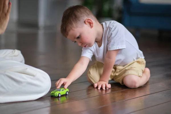 Uttrycksfull pojke leker med en leksaksbil med mamma i bakgrunden — Stockfoto