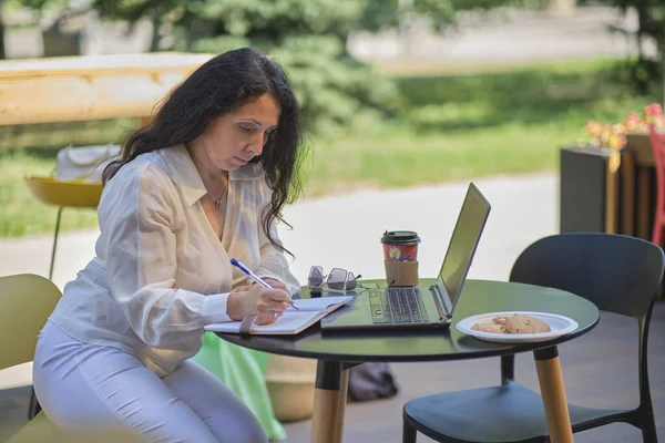 Mulher madura no café. Retrato de mulher profissional madura confiante sentado no terraço de verão no café, usando computador portátil para o trabalho, rindo alegremente dentro de casa. — Fotografia de Stock