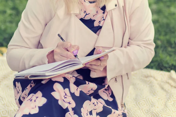 Menina com caneta escrita no notebook na grama fora . — Fotografia de Stock