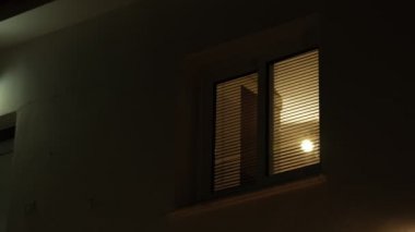 Gecenin karanlığında evin penceresinden gelen ışık. Oda aydınlanıyor ve kapanıyor..