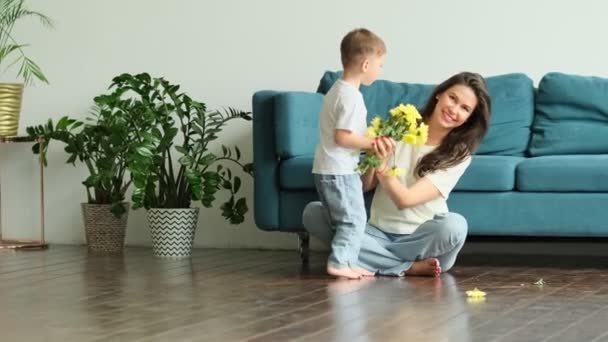 Grattis på mors dag. barn son gratulerar mor på semester och ger blommor. Grattis till mödradagen under semestern hemma — Stockvideo
