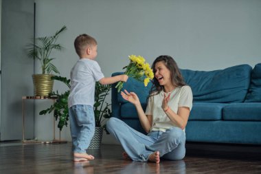 Anneler Günün kutlu olsun. Çocuk evlat tatilde annesini tebrik eder ve çiçek verir. Evde bayram kutlamaları sırasında anneler günü için onu tebrik etmek.