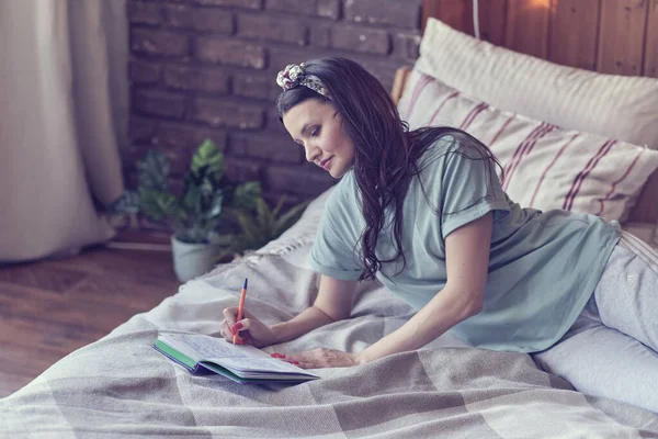 Életmód puha kép csinos fiatal nő ül a hangulatos ágyban, és jegyzetel a naplójába. Őszi szezonhangulat. — Stock Fotó