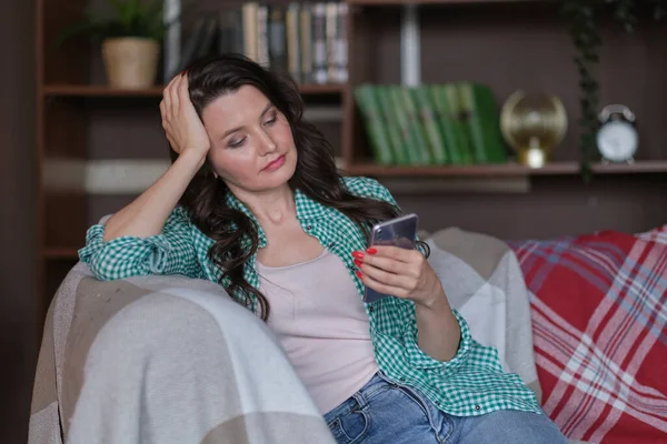 Frau sitzt mit Handy zu Hause auf der Couch und sieht traurig aus — Stockfoto