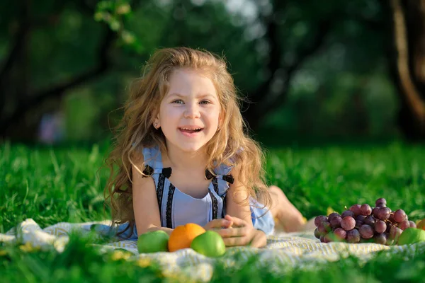 Ευτυχισμένο κοριτσάκι που διασκεδάζει στο πάρκο. Χαριτωμένο παιδί κάθεται στο γρασίδι σε μια ηλιόλουστη μέρα του καλοκαιριού. — Φωτογραφία Αρχείου
