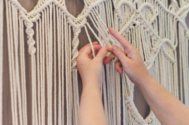 Makrome 'un temel düğümleri, kadın elinin omuz arkasının görüntüsü, düğümleniyor. Çevre dostu modern örgü doğal dekorasyon konsepti.