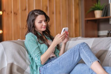 Orta yaşlı bir kadın evde, koltukta tüketim yapıyor..