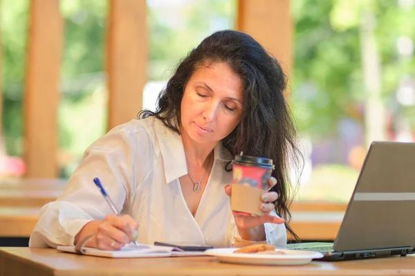 Retrato de bela empresária sênior sentada no café com laptop olhando para o lado e pensando. Mulher madura no café. rindo alegremente dentro de casa. — Fotografia de Stock