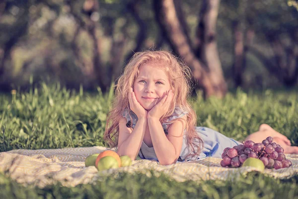 Счастливая маленькая девочка развлекается в парке. Симпатичный ребенок сидит на траве в солнечный летний день. — стоковое фото