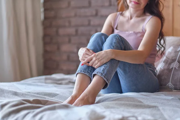 Mulheres irreconhecíveis a vestir calças de ganga sentadas a abraçar os joelhos na cama. depressão, conceito de solidão — Fotografia de Stock
