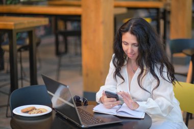 Kahve dükkanındaki olgun kadın. Yazlık terasta oturan kendine güvenen profesyonel bir kadının portresi, iş için dizüstü bilgisayar kullanması, kapalı alanda mutlu bir şekilde gülmesi..