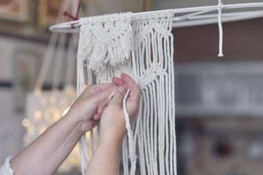 Makrome 'un temel düğümleri, kadın elinin omuz arkasının görüntüsü, düğümleniyor. Çevre dostu modern örgü doğal dekorasyon konsepti.