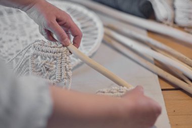 Yaratıcı bir masaüstü üzerinde aletlerle özel makrome dekor üzerinde çalışan bir kadın yukarıdan izleniyor. Hobi örgü örme el ve iplik makromu.