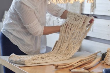 Yaratıcı bir masaüstü üzerinde aletlerle özel makrome dekor üzerinde çalışan bir kadın yukarıdan izleniyor. Hobi örgü örme el ve iplik makromu.