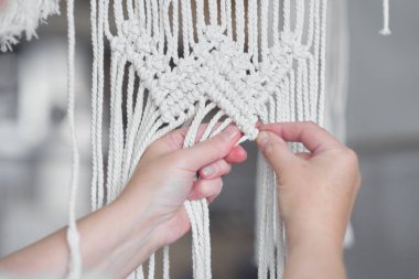 Makrome 'un temel düğümleri, kadın elinin omuz arkasının görüntüsü, düğümleniyor. Çevre dostu modern örgü doğal dekorasyon konsepti.