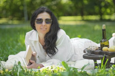 Kendinden emin olgun bir kadının portresi. Gülümseyen kadın kameraya sırıtarak bakıyor. Başarılı orta yaşlı kadın parkta dinleniyor..