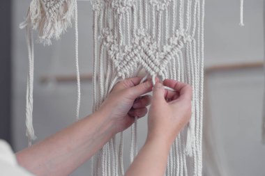 Makrome 'un temel düğümleri, kadın elinin omuz arkasının görüntüsü, düğümleniyor. Çevre dostu modern örgü doğal dekorasyon konsepti.