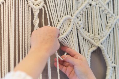 Makrome 'un temel düğümleri, kadın elinin omuz arkasının görüntüsü, düğümleniyor. Çevre dostu modern örgü doğal dekorasyon konsepti.