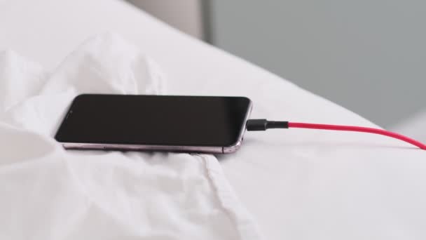 Smartphone deitado na cama em folhas brancas amassadas cobrando pela manhã, close-up. Fundo do quarto. Deixando um dispositivo de telefone autônomo, cobrando conceito abstrato durante a noite — Vídeo de Stock