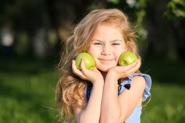 La niñita sonríe a la cámara. chica bonita posando para una foto y sosteniendo dos manzanas verdes frescas en sus manos — Foto de Stock