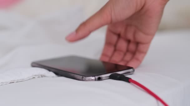 Smart phone is opladen op het bed en liggen op witte stof. Smartphone verslaafde en gezonde levensstijl concept. USB-kabel verbonden met een witte mobiele telefoon — Stockvideo