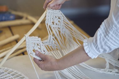 Yaratıcı bir masaüstü üzerinde aletlerle özel makrome dekor üzerinde çalışan bir kadın yukarıdan izleniyor. Hobi örgü örme el ve iplik makromu.