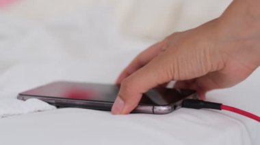 Akıllı telefon yatakta şarj oluyor ve beyaz kumaşın üzerinde yatıyor. Akıllı telefon bağımlısı ve sağlıklı yaşam tarzı konsepti. USB kablosu beyaz bir cep telefonuna bağlandı