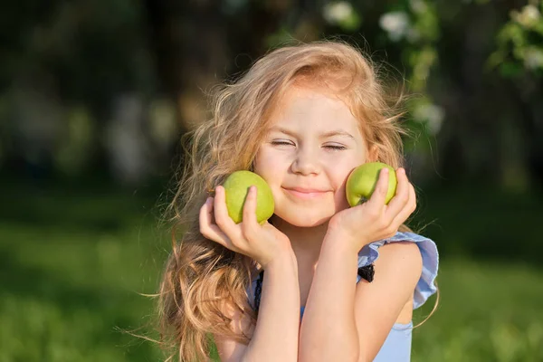 Dziewczynka uśmiecha się do kamery. ładna dziewczyna pozowanie do zdjęcia i trzymając dwa zielone świeże jabłka w jej rękach — Zdjęcie stockowe