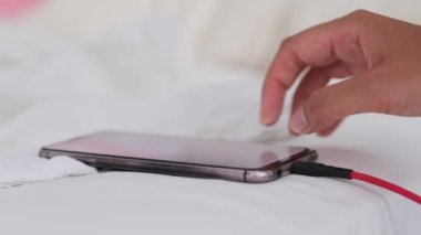Akıllı telefon kırışık beyaz çarşaflar içinde yatakta uzanıyor, sabahları şarj oluyor, kapanıyor. Yatak odası arka planı. Bir telefon cihazını başıboş bırakmak, soyut kavramları şarj etmek.