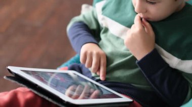 Kanepede oturup tablet kullanırken gülümseyen neşeli küçük çocuk. Modern çocuk ve eğitim teknolojisi. Küçük çocuk evdeki dokunmatik yere bakıyor..