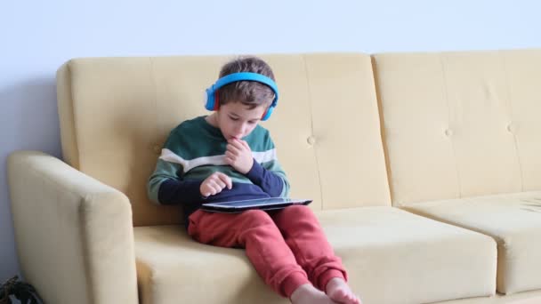 Ragazzino allegro che sorride sdraiato sul divano e usa tablet a casa. Ragazzo moderno e tecnologia educativa. bambino guardando touch pad a casa. — Video Stock