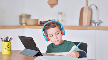 Akıllı çocuk tablet hakkında online ders dinliyor kulaklık takıyor Spbas. Evde eğitim görmüş çocuk gözetimi.