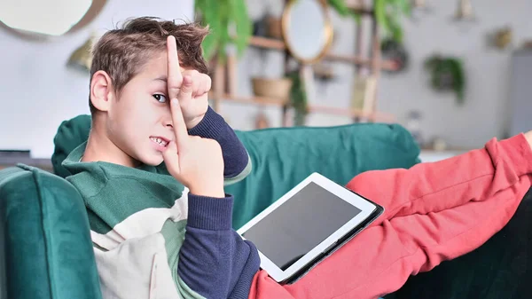 Cheerful little boy smiling while sitting on couch and using tablet at home. Modern kid and education technology. little boy looking at touch pad at home. — Stock Photo, Image