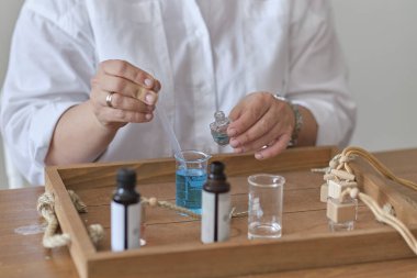 Yağlı ve cam şişeli bir pipetin yakın çekimi. Kadın şişeye parfüm döküyor. Parfüm atölyesi oluşturma