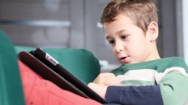 Modern nesil. Çocuk İPad 'de oynuyor. Küçük çocuk evde dijital tabletle oynarken gülümsüyor. Modern çocuk ve eğitim teknolojisi. Küçük çocuk evdeki dokunmatik yere bakıyor..